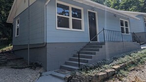 A single-story house with a front porch, a staircase, and a small front yard. - Cozy Cottage Cabin #1 (Bull Shoals)