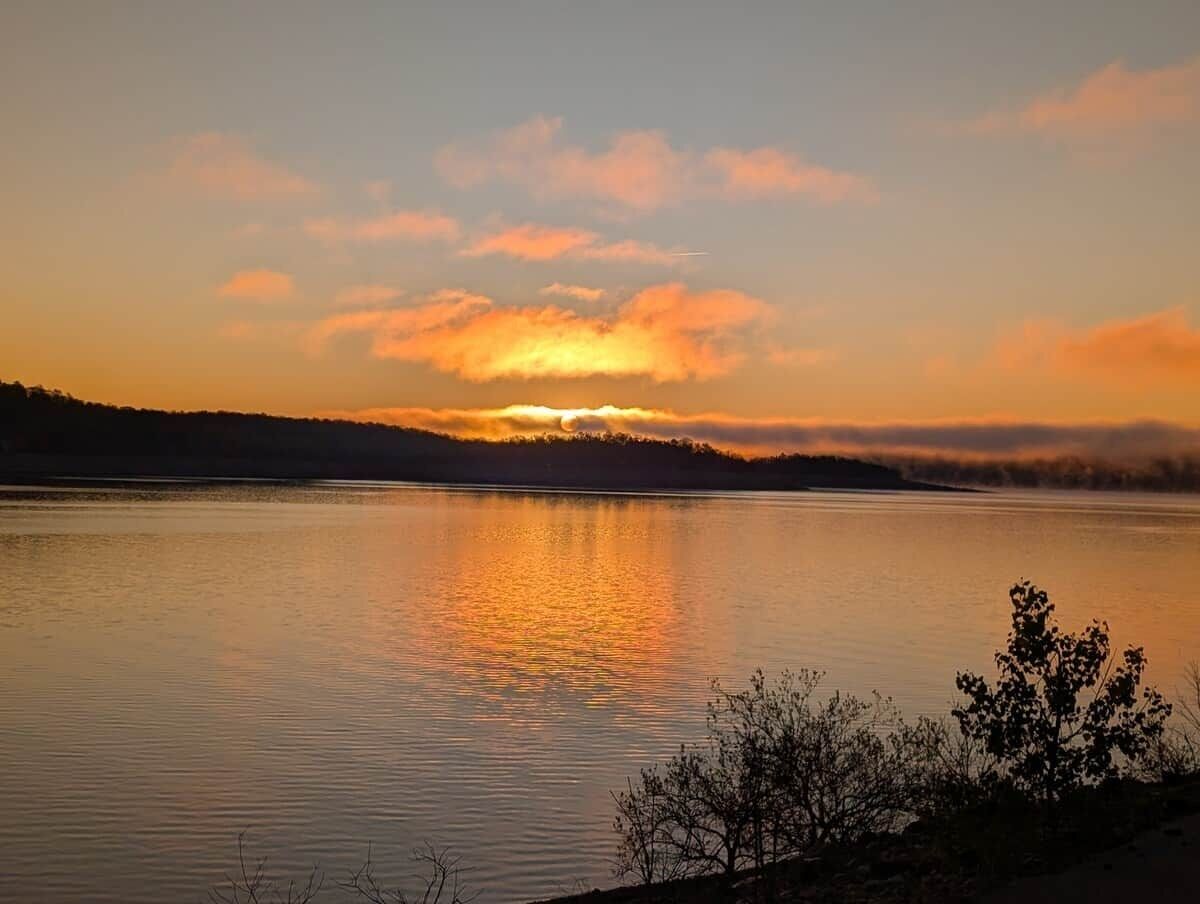 Tyyni järvi auringonlaskun aikaan, sen rannalla metsä.