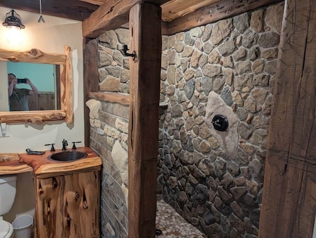 A rustic bathroom with a stone wall, wooden beams, a sink, and a mirror.. Cozy Lakeside Cabin #4
