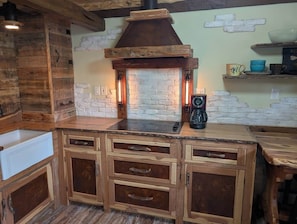A rustic kitchen with wooden cabinets, a stone fireplace, and a coffee maker.