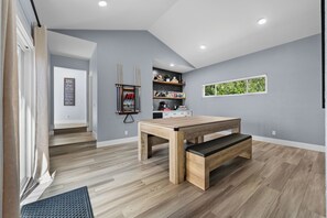 Eine moderne Küche mit Holztisch und Bank, grauen Wänden und einem Fenster mit Grünpflanzen draußen.
