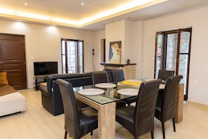 Una sala de estar moderna con un sofá, una mesa de comedor, sillas, un televisor de pantalla plana y una chimenea.