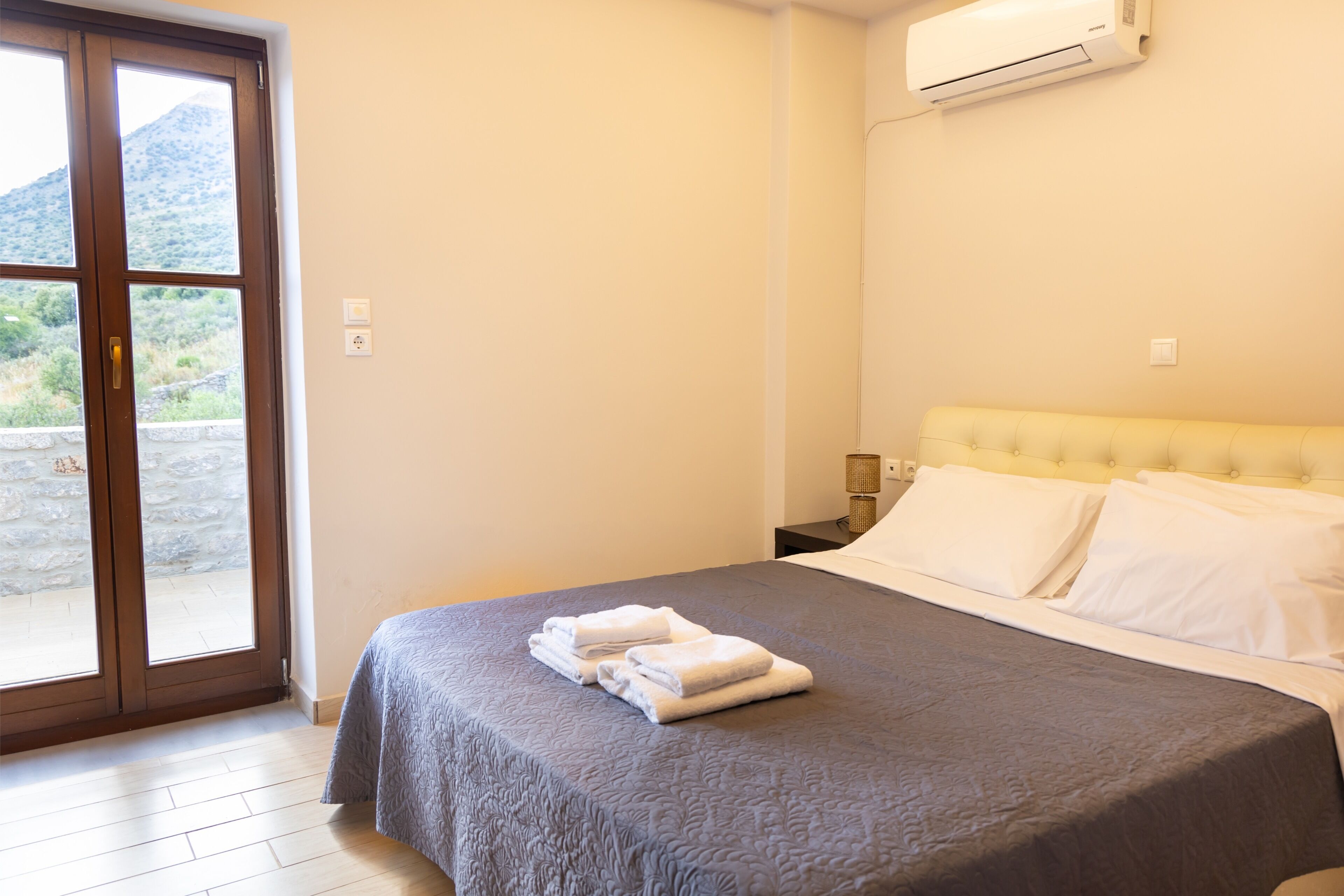 A hotel room with a bed, a window with a view of a mountain, and an air conditioning unit.