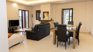 A modern living room with a fireplace, a dining table with chairs, a sofa, and a television. - Mani Stone Tower– Sea & Mountain Escape by ΜΡS (Oitylo)