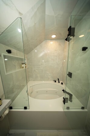 Casa de banho moderna com banheira de hidromassagem em vidro, paredes de mármore e cabine de duche em vidro.