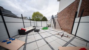 Een terras met een bank, een kleine tafel en een speelruimte met groen.
