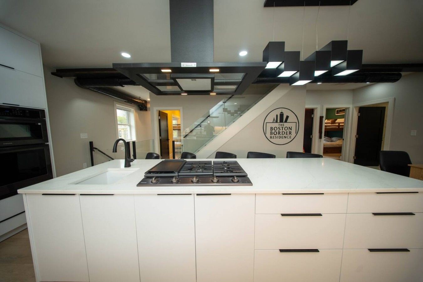 A modern kitchen with a central island, a built-in oven, and a staircase leading to an upper level.