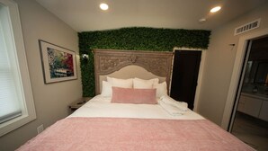 Een hotelkamer met een bed, een hoofdeinde tegen een groene muur, een schilderij aan de muur en een deur aan de rechterkant.