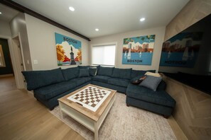 Ein Wohnzimmer mit einem Ecksofa, einem Couchtisch mit Schachbrett und drei Wandbildern, die Boston zeigen.