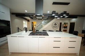 A modern kitchen with a central island, built-in oven, and a staircase leading to another level. - Boston Themed Luxury Stay w Hot tub and Jacuzzi (Medford)