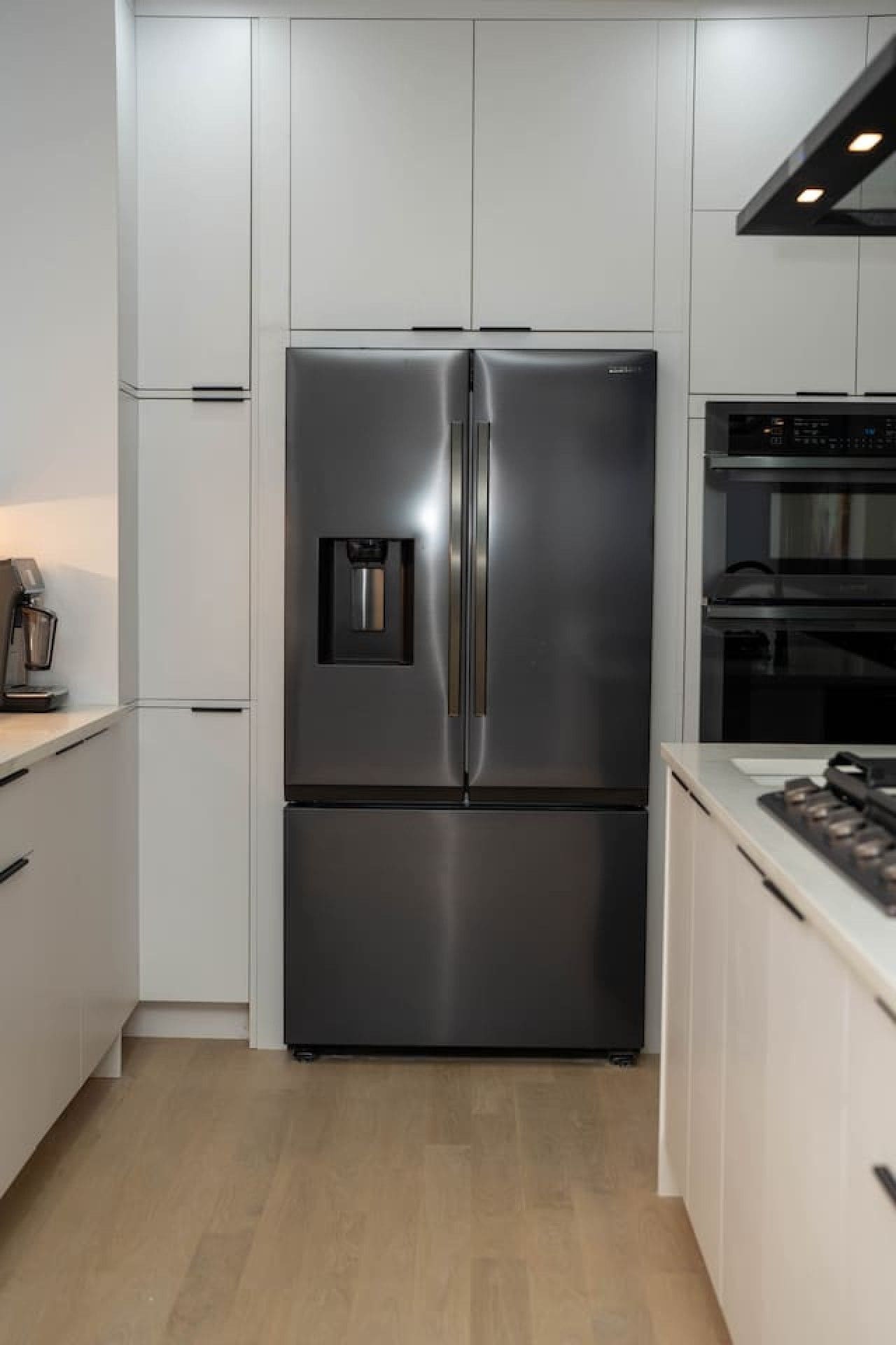 Een moderne keuken met een roestvrijstalen koelkast met dubbele deuren, een inbouwoven en een koffieapparaat.