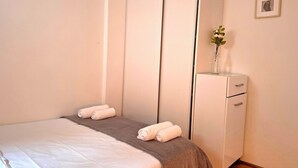 Une chambre à coucher avec un lit, une commode et un petit vase avec des fleurs posé sur la commode.