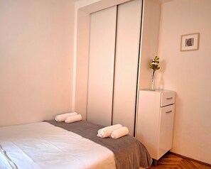 A bedroom with a bed, a dresser, and a small vase with flowers on the dresser. - Apartment with sea view, separate entrance, private terrace, parking & BBQ courtyard (Petrovac na moru)