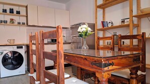 Un coin repas avec une table et des chaises en bois, un vase avec des fleurs et, au fond, un lave-linge.