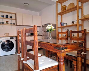 A dining area with a wooden table and chairs, a vase with flowers, and a washing machine in the background. - Apartment with sea view, separate entrance, private terrace, parking & BBQ courtyard (Petrovac na moru)