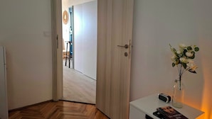 Une pièce avec un plancher en bois, une porte blanche, une petite table sur laquelle se trouve un vase de fleurs et un livre.