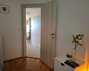 A room with a wooden floor, a white door, a small table with a vase of flowers, and a book. - Apartment with sea view, separate entrance, private terrace, parking & BBQ courtyard (Petrovac na moru)