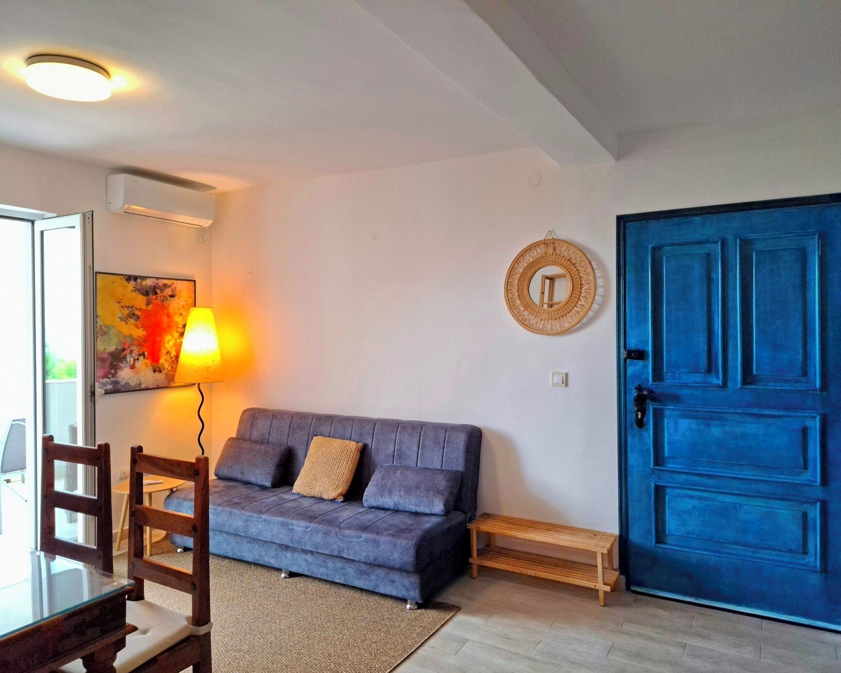 Un salon avec une porte bleue, un canapé, une lampe et un miroir fixé au mur.