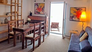 Un salon avec un piano, une table à manger entourée de chaises, un canapé et deux tableaux accrochés au mur.