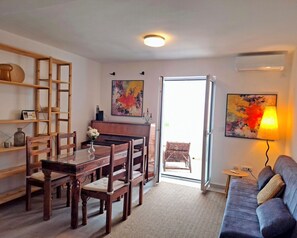 A living room with a piano, a dining table with chairs, a sofa, and two paintings on the wall. - Apartment with sea view, separate entrance, private terrace, parking & BBQ courtyard (Petrovac na moru)