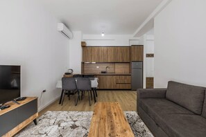 Ett modernt vardagsrum med en platt-TV, en grå soffa och ett soffbord i trä.