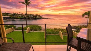 Ein Balkon mit Blick auf einen Sonnenuntergang über dem Meer, eine Rasenfläche und Korbmöbel.