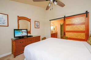 A bedroom with a bed, a television on a wooden dresser, a ceiling fan, a mirror, and a sliding door leading to a bathroom. - Napili Point 2 Oceanfront Villas, Sleeps 12 | Car Incl. w/ 6 nights | ML-4062 by KBM (Lahaina)
