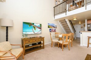 A living room with a TV, wooden furniture, a dining table, and a staircase leading to an upper level. - Napili Point 2 Oceanfront Villas, Sleeps 12 | Car Incl. w/ 6 nights | ML-4062 by KBM (Lahaina)