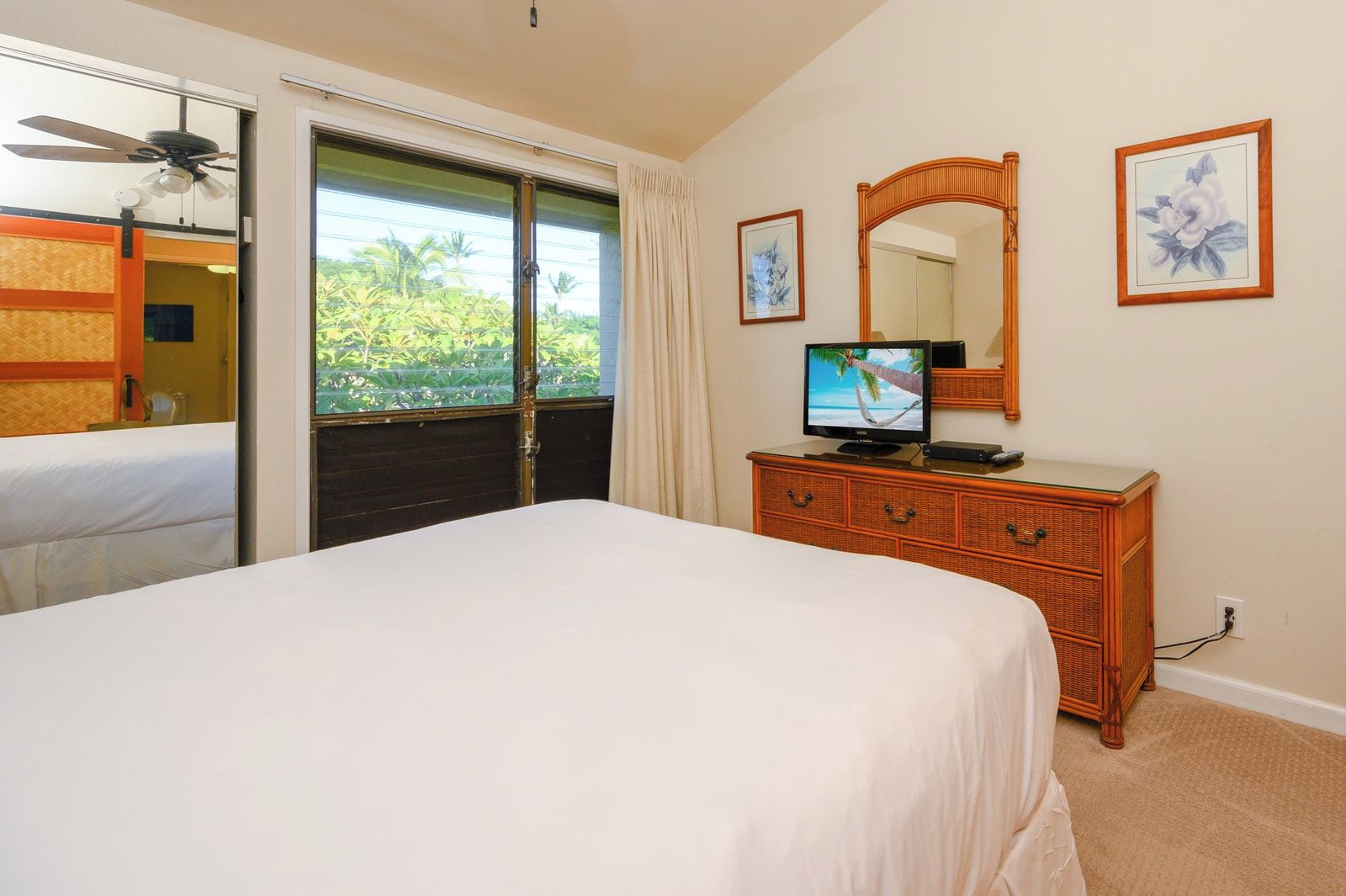 Un dormitorio con cama, cómoda, televisor, espejo y puerta corrediza a un balcón.