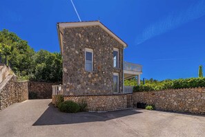 Ein zweistöckiges Steinhaus mit Balkon, gepflasterter Auffahrt und Steinmauer.