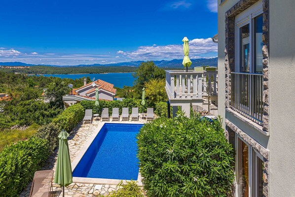 Ein Pool mit freiem Blick auf das Meer und die dahinterliegenden Berge.