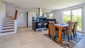 Een moderne keuken met een centraal eiland, een eethoek met een tafel en stoelen, en een trap.