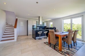 Eine moderne Küche mit Kochinsel, einem Essbereich mit Tisch und Stühlen sowie einer Treppe.