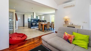 Een moderne woonkamer met een bank, een rode relaxfauteuil en een eethoek met een tafel en stoelen.