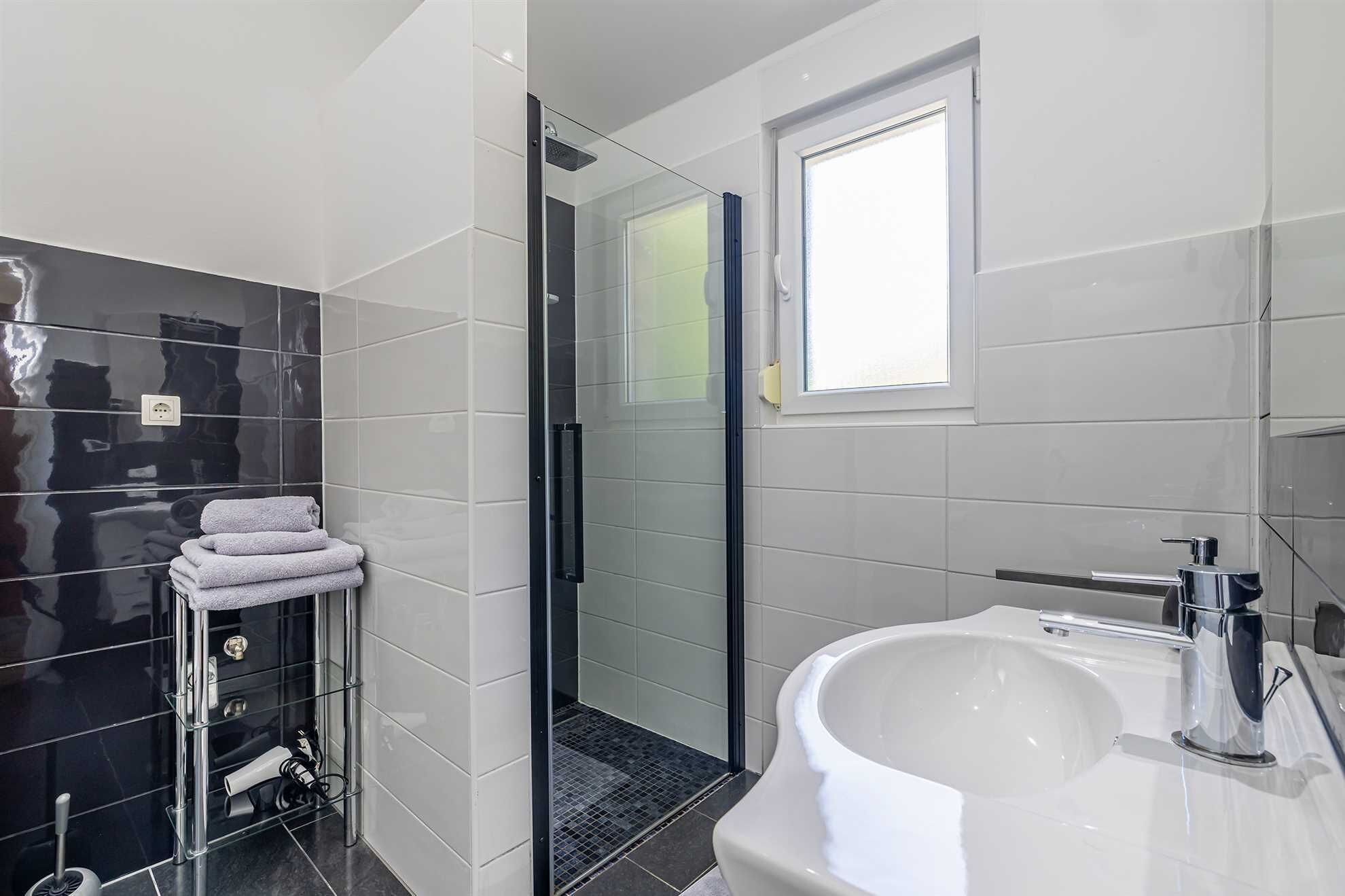 A modern bathroom with a glass-enclosed shower, a white sink, and a towel rack.
