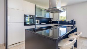 Een moderne keuken met een centraal eiland, roestvrijstalen apparatuur en een groot raam.