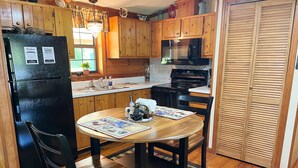 Una cocina con armarios de madera, un refrigerador negro, un microondas y una mesa de comedor con sillas.
