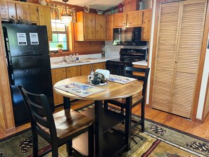 A kitchen with wooden cabinets, a black refrigerator, a microwave, and a dining table with chairs.