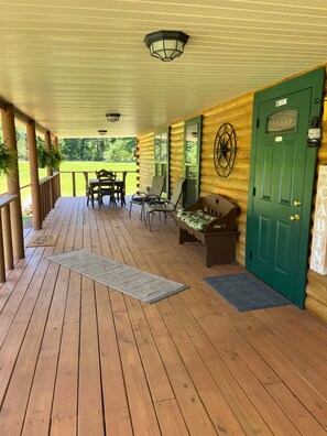 A covered porch with wooden flooring, a green door, and a table with chairs.