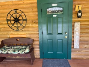 A wooden cabin interior with a green door, a compass wall decoration, a bed with a leaf-patterned mattress, and a welcome sign.