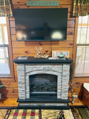 A fireplace with a stone surround, a mounted television above it, and a sign above the TV that reads 'LIFE IS GOOD'.