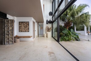 Ein modernes Interieur mit einer Diele, einem großen Fenster und einem Palmenbaum vor der Fensterfront.