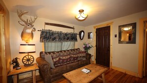 Una sala de estar acogedora con suelo de madera, un sofá de cuero, una mesa de centro de madera, una cabeza de venado decorativa en la pared, una lámpara y un espejo.