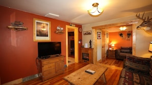 Una sala de estar con televisor, muebles de madera, chimenea y decoración de cabeza de venado.