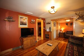 Ein Wohnzimmer mit Fernseher, Holzmöbeln, Kamin und Dekoration mit einem Hirschkopf.