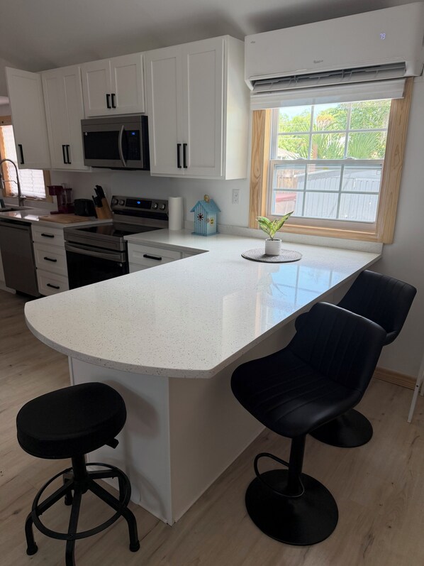 A kitchen with white cabinets, a microwave, a stove, and a large island with bar stools.
