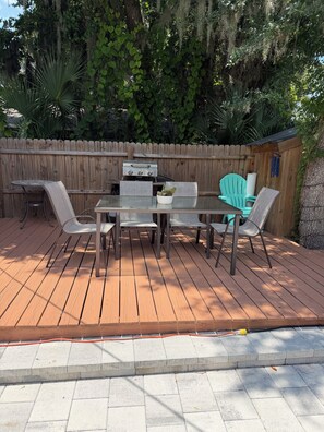Eine Terrasse im Freien mit Holzdeck, Grill und Tisch mit Stühlen.