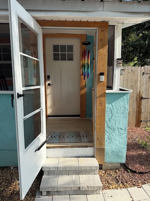 A house entrance with a white door, a welcome mat, and a wooden fence.