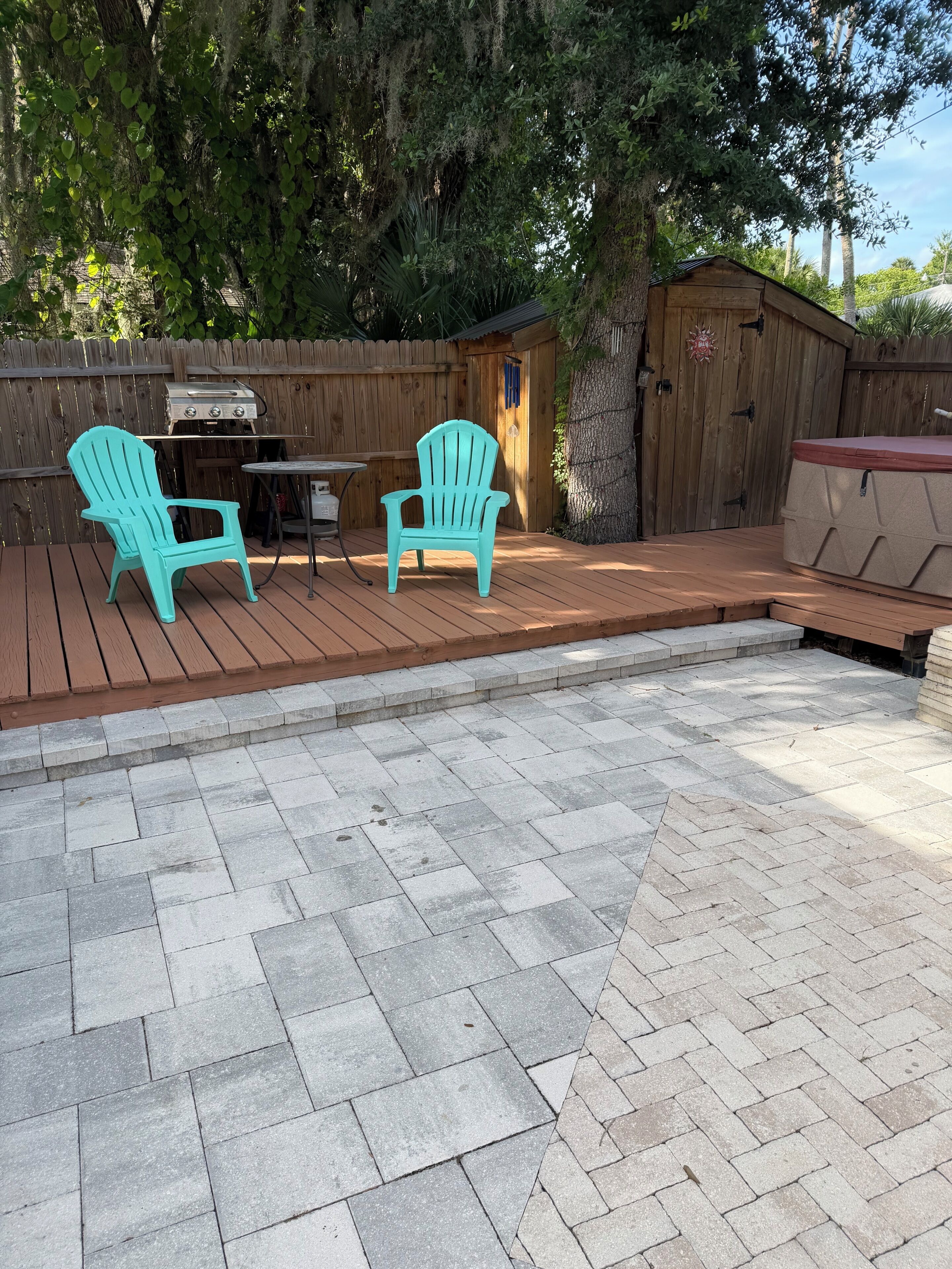 A patio with two Adirondack chairs, a grill, and a small shed.