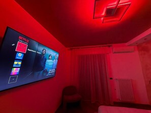 Ett rum med en tv-skärm som visar Netflix-gränssnittet, en röd vägg, ett fönster med gardiner och ett element.